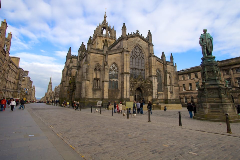 A historic cathedral with intricate Gothic architecture, a statue, and a cobblestone square.