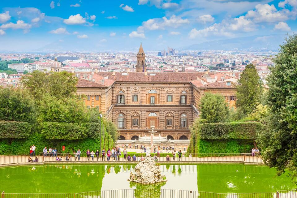 Un edificio histórico con una fuente central, rodeado de un jardín formal y un gran estanque.