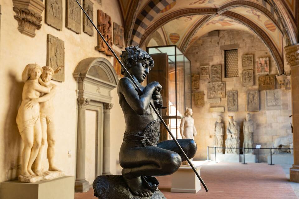 A statue of a seated figure holding a staff in a historical building with arches and classical sculptures.