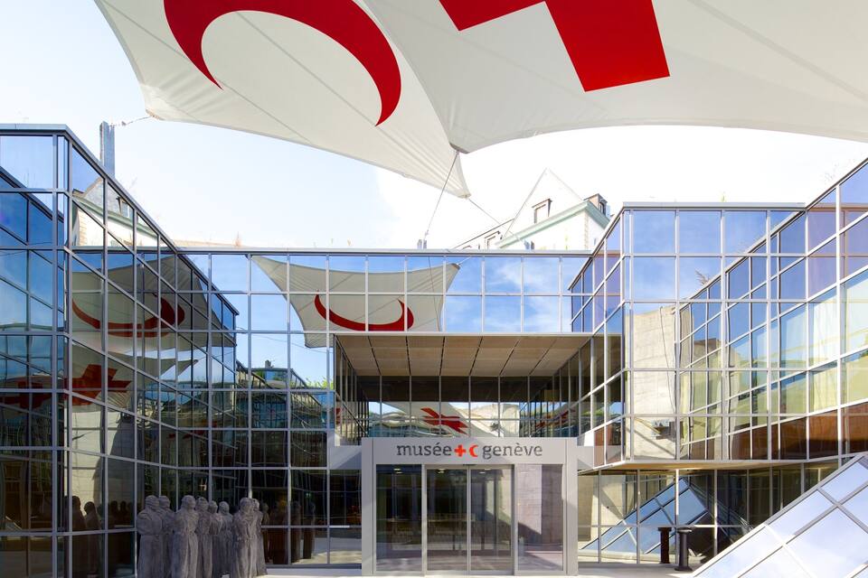 A modern glass building with a large red and white logo, and the sign 'musée+cgenève'.