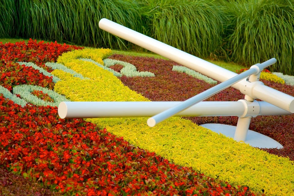 A sculpture of a seesaw in a garden with colorful flower beds.