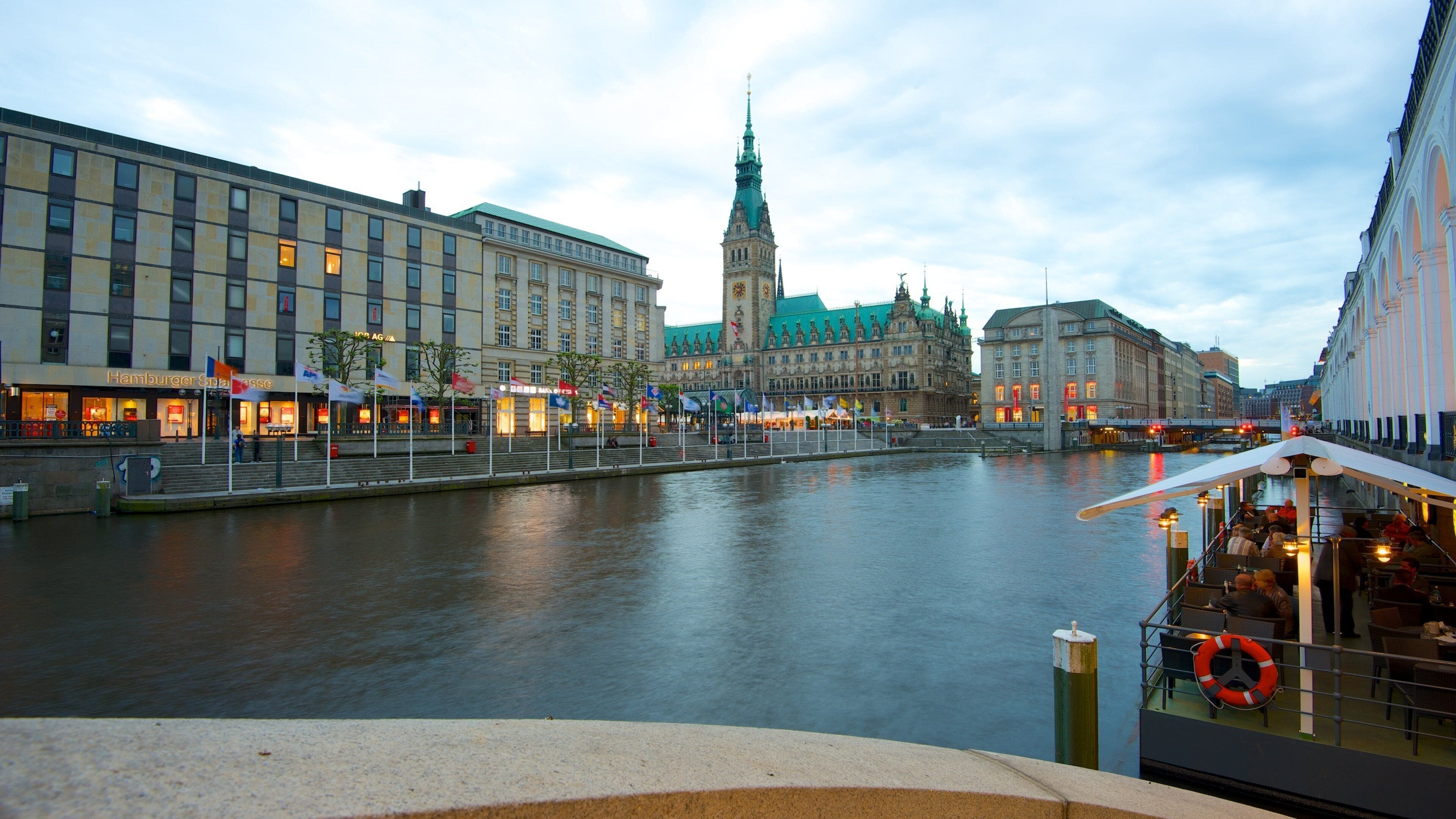 A river with buildings on both sides, a prominent tower, and a boat with people on it.