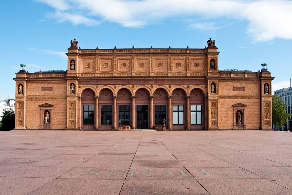 A large, historic building with a central arched entrance and statues on either side.