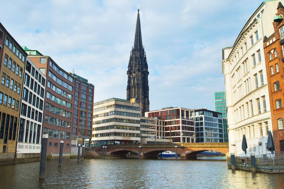 Un río con edificios modernos y la aguja de una iglesia histórica.