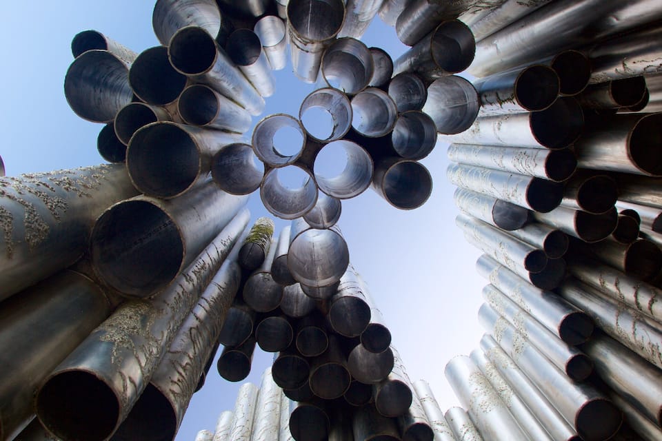 A large collection of cylindrical metal pipes arranged in a circular pattern against a clear sky.