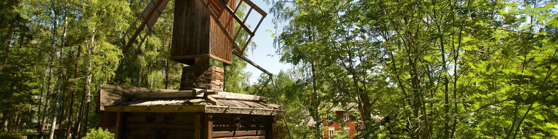 A traditional wooden windmill surrounded by lush green trees.