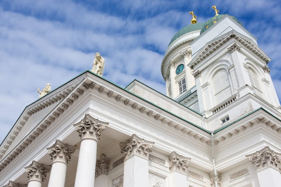 A white building with ornate columns and a green dome.