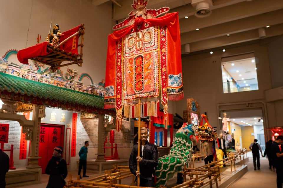 A traditional Chinese temple with red and gold decorations, a lion dance, and visitors.