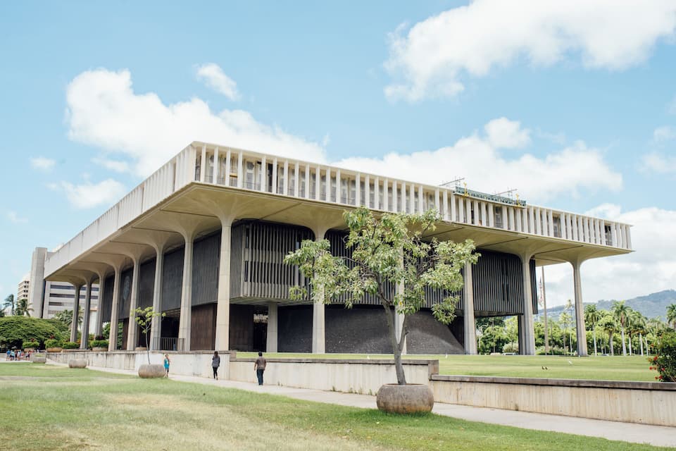 Un bâtiment moderne doté d’un toit plat et de colonnes, entouré d’une pelouse bien entretenue et d’arbres.