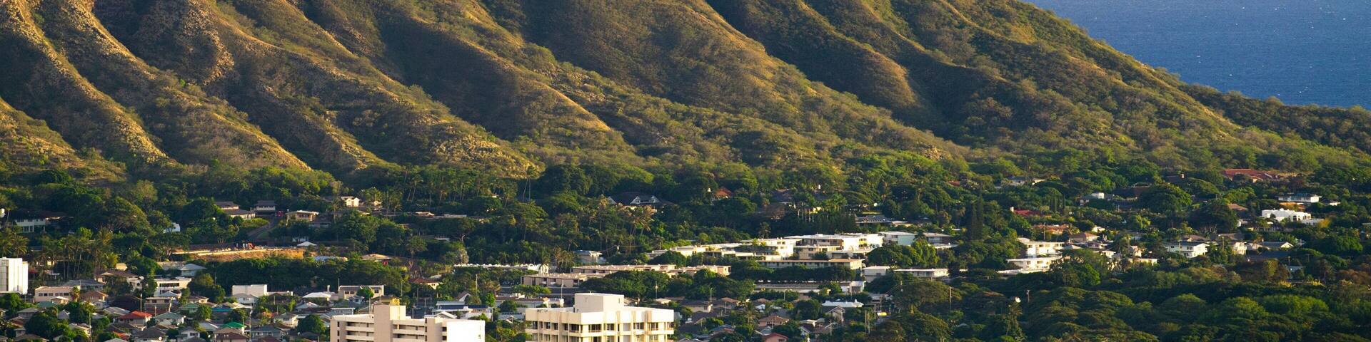 A mountain with a peak, surrounded by greenery and a coastal town.