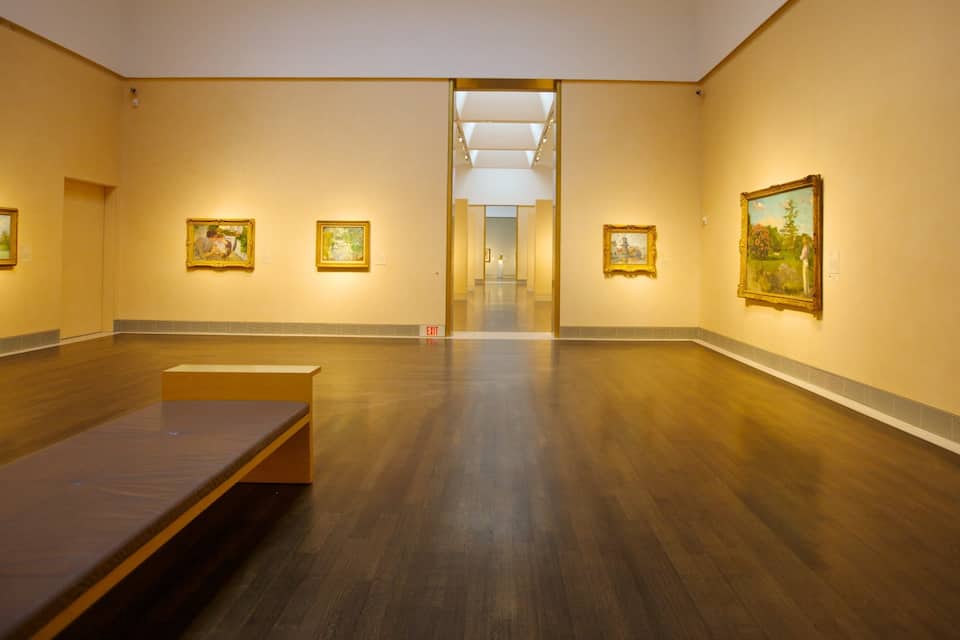 Een kunstgalerie met houten vloeren en wanden, met verschillende ingelijste schilderijen.