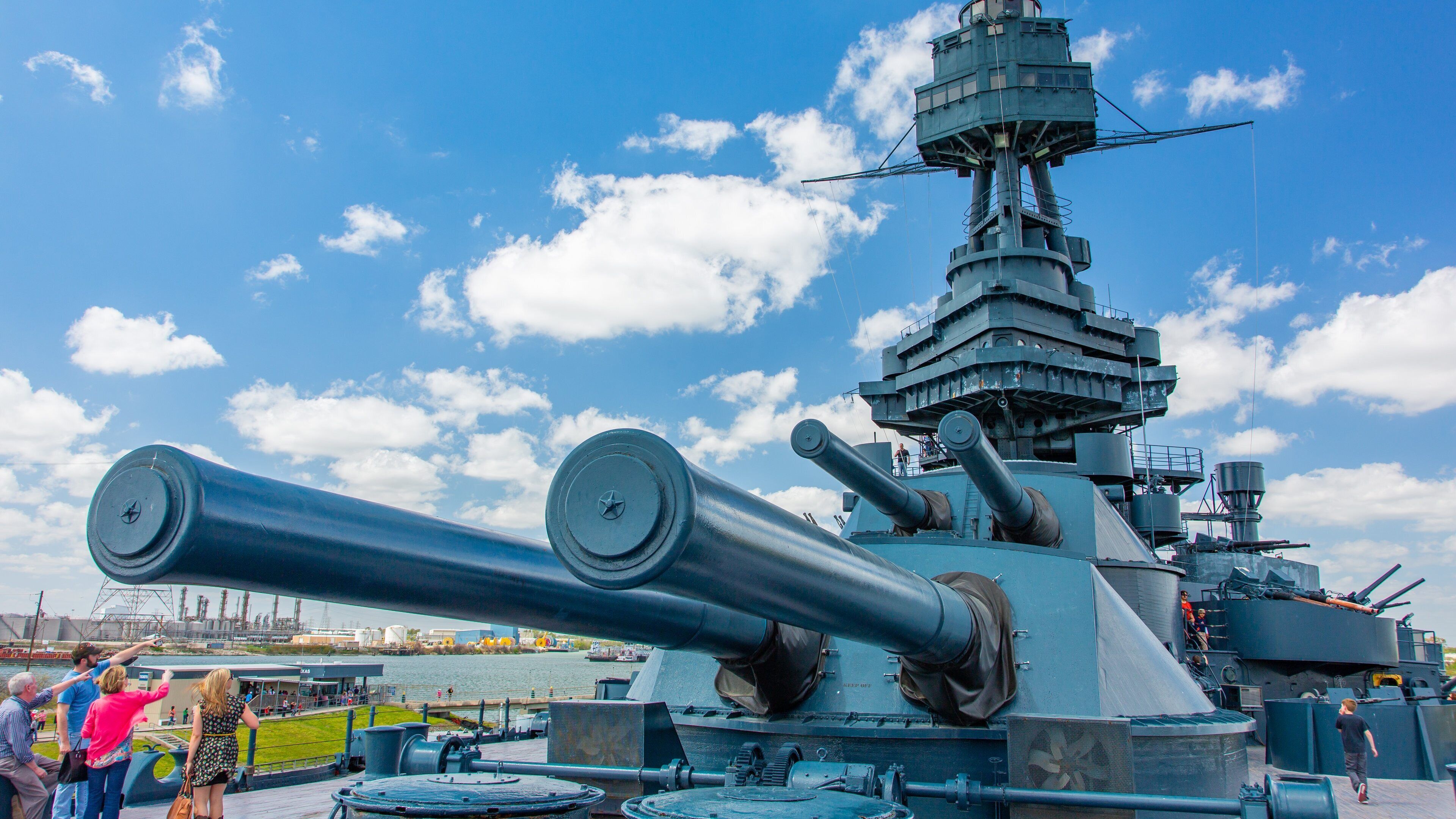 A large naval gun turret on a ship with a clear sky and clouds in the background.