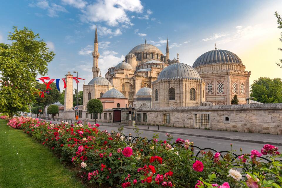 Une mosquée historique, dotée de plusieurs dômes et minarets, entourée d’un jardin bien entretenu où s’épanouissent de magnifiques fleurs.