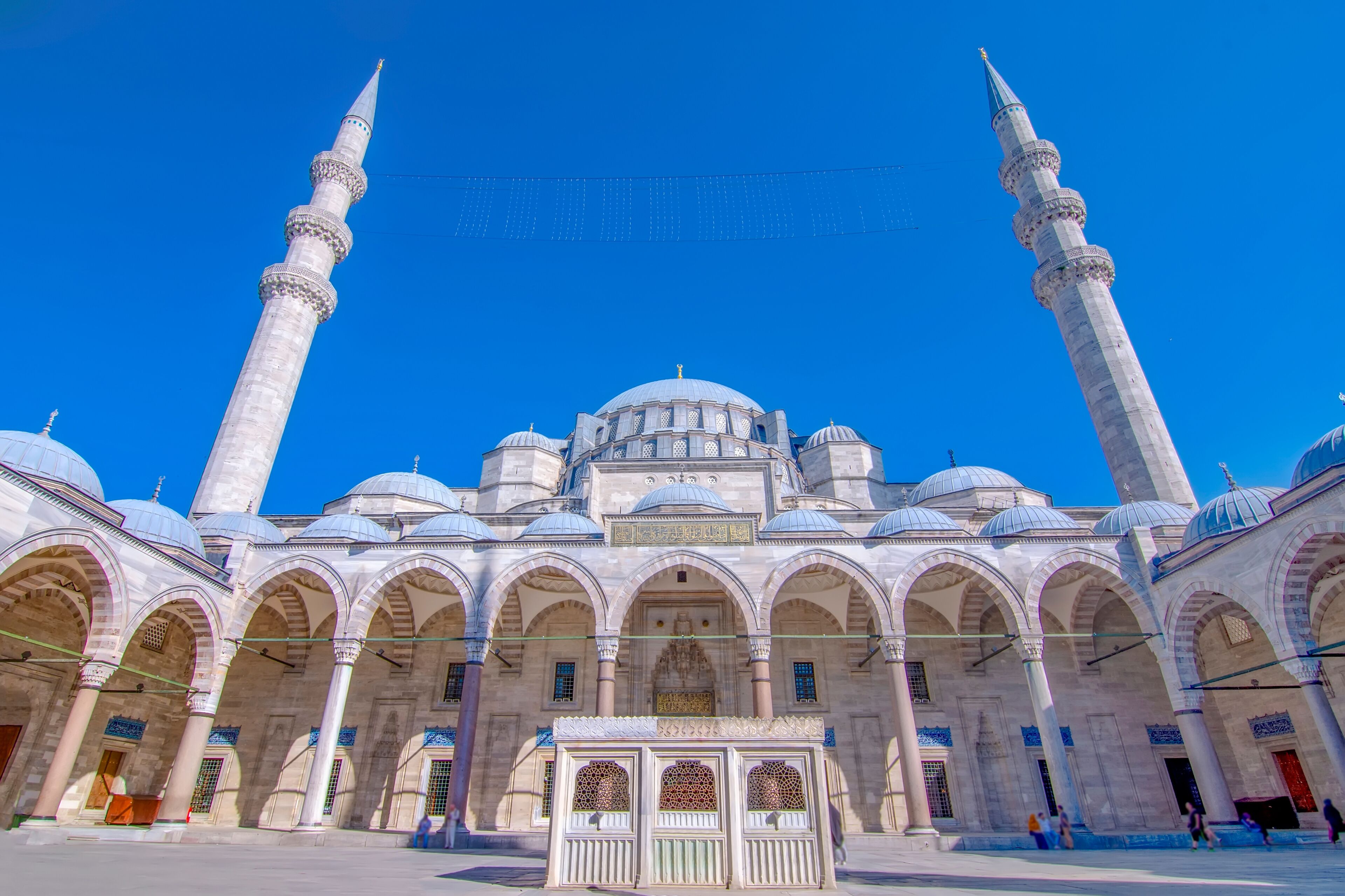 A historic mosque with multiple domes and minarets, featuring intricate architectural details and a clear blue sky.