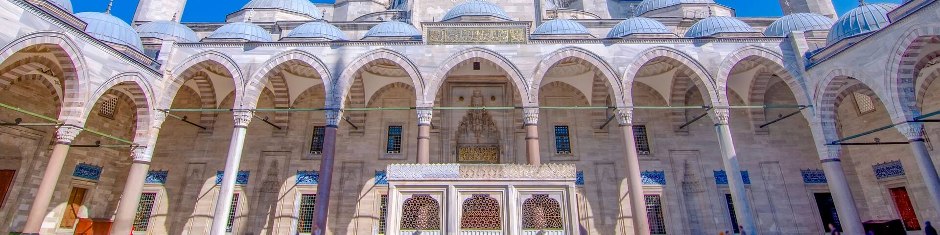 A historic mosque with multiple domes and minarets, featuring intricate architectural details and a clear blue sky.