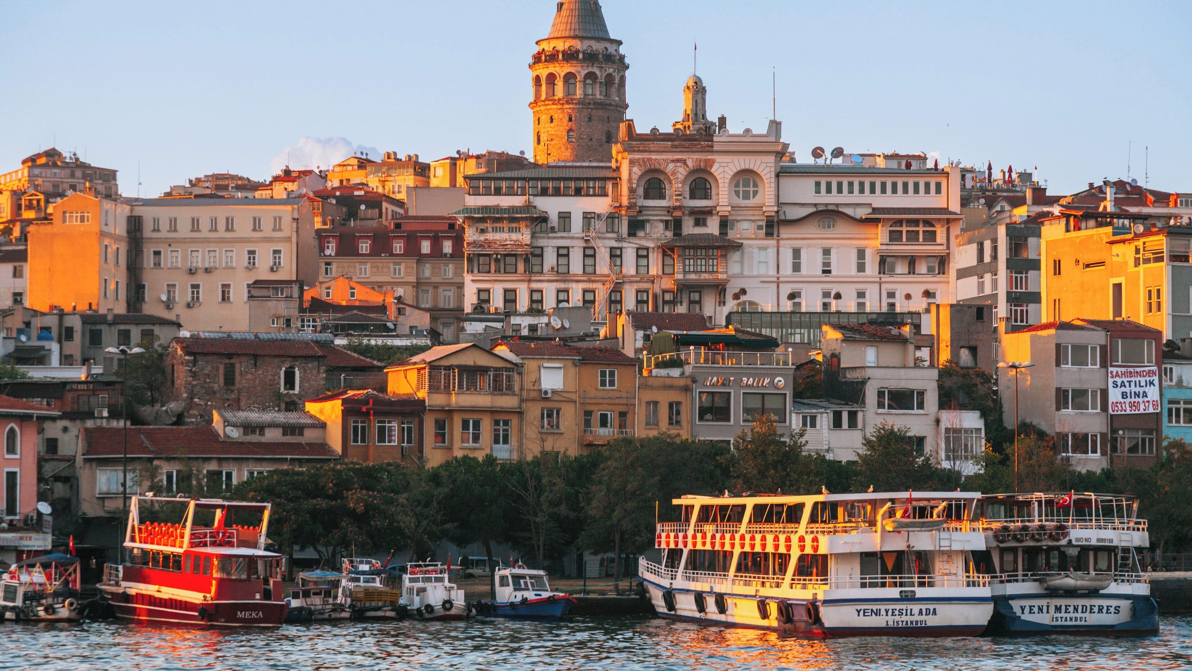 Sunset view of Galata Tower overlooking colorful buildings and boats in the Istanbul city center