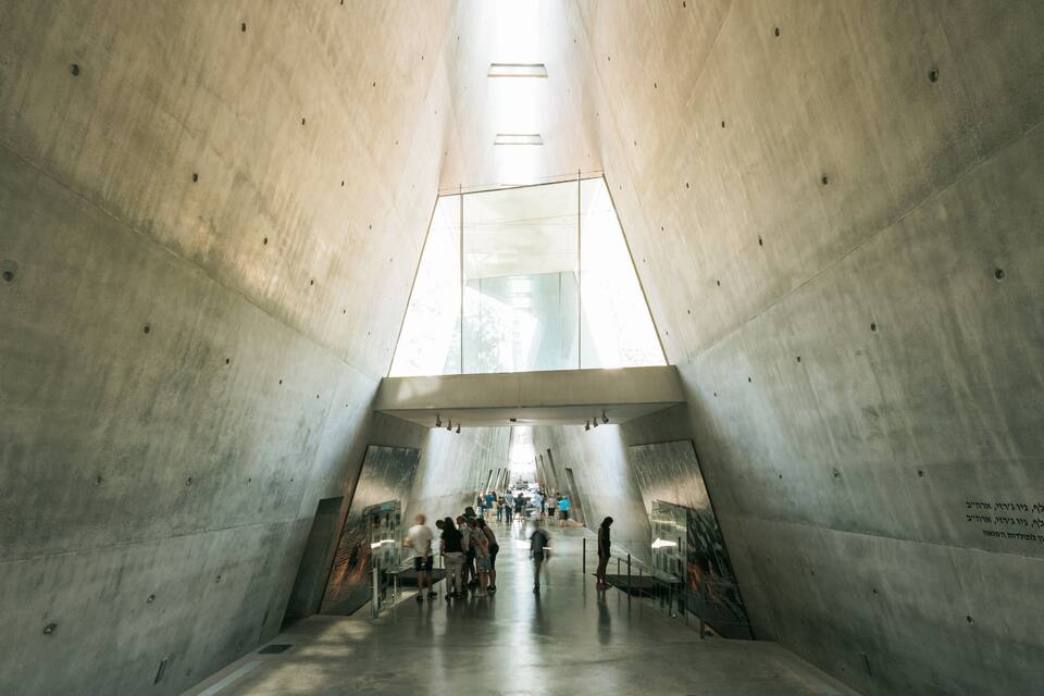 A modern architectural structure with a central glass window and visitors inside.
