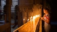 A woman lighting candles in a church with ornate columns and a religious painting in the background.