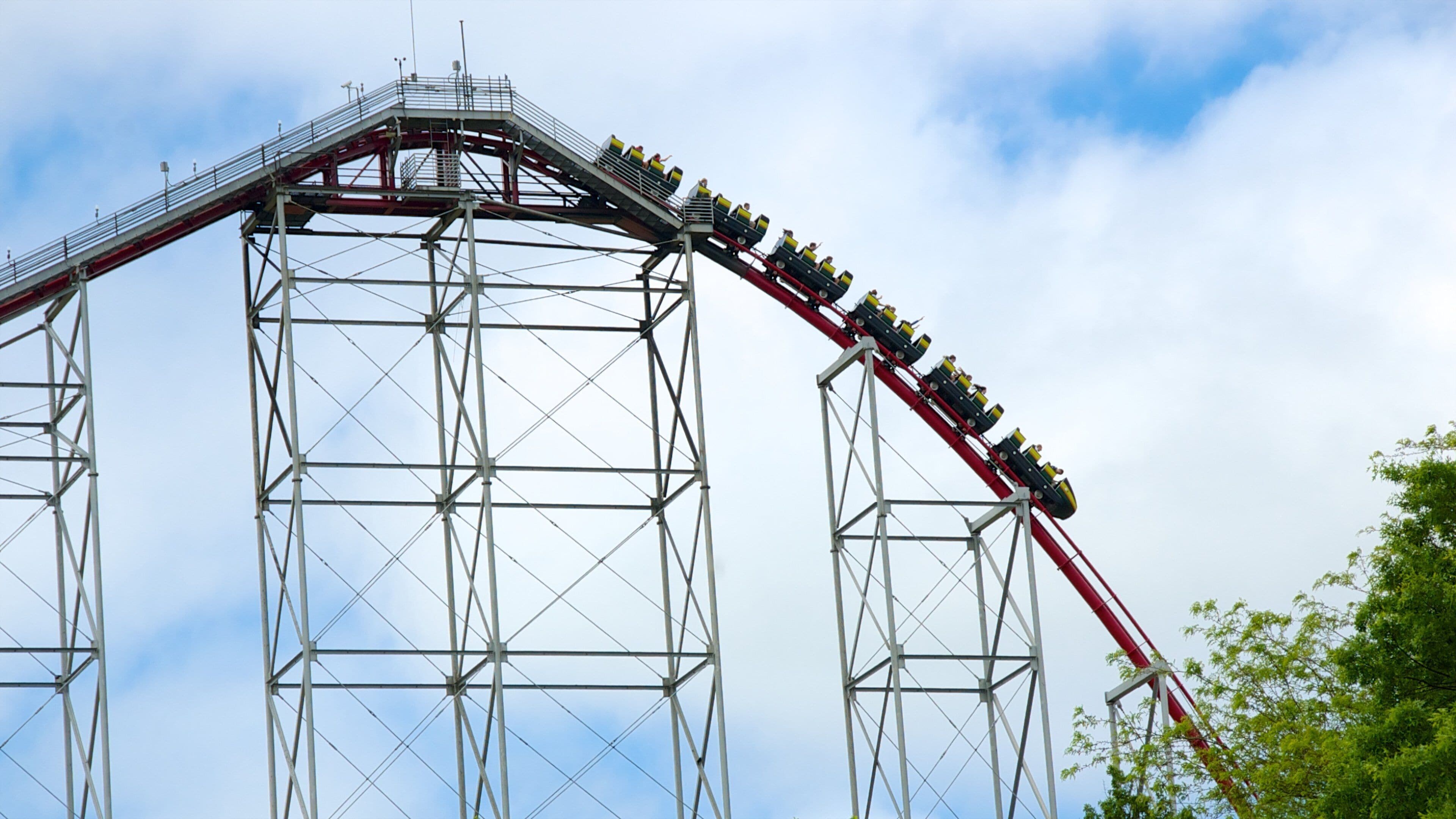 A roller coaster with multiple cars in motion, supported by a steel framework, against a partly cloudy sky.