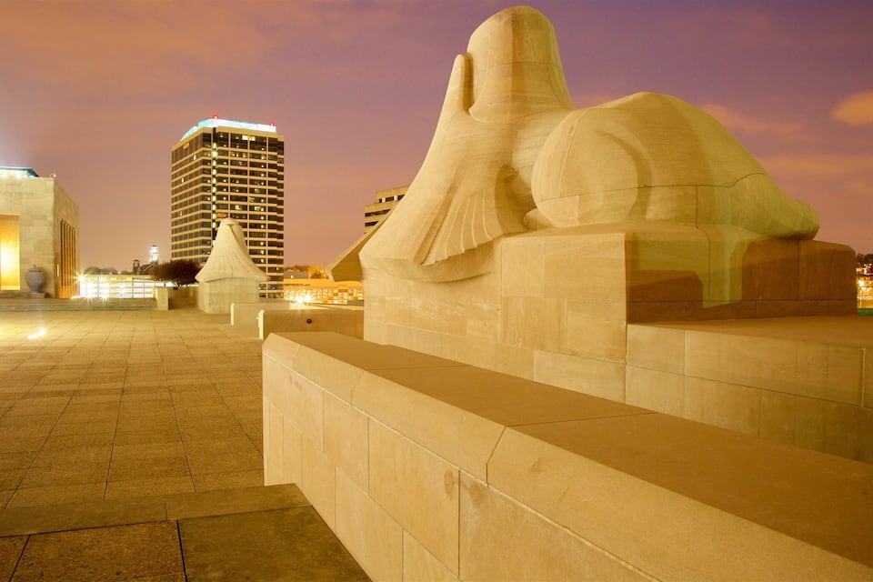 Grande escultura de pedra de uma figura reclinada em ambiente urbano à noite.