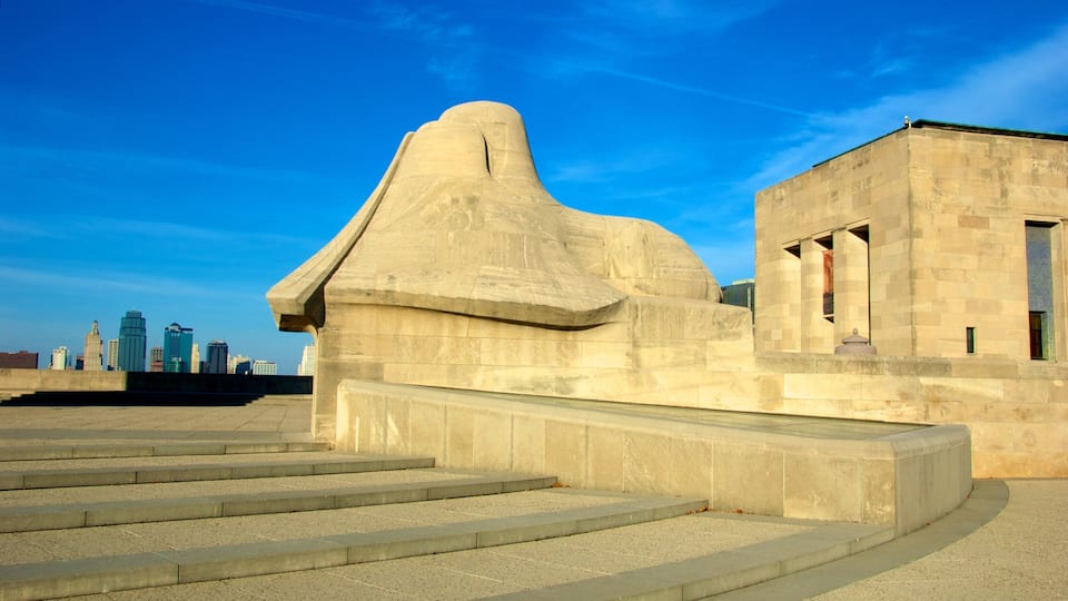 A large stone monument with a unique shape, a set of stairs leading up to it, and a modern city skyline in the background.