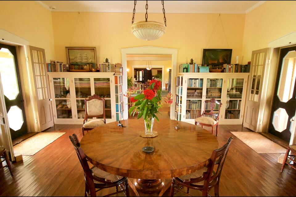 A dining room with a wooden table, chairs, a vase with flowers, and bookshelves filled with books.