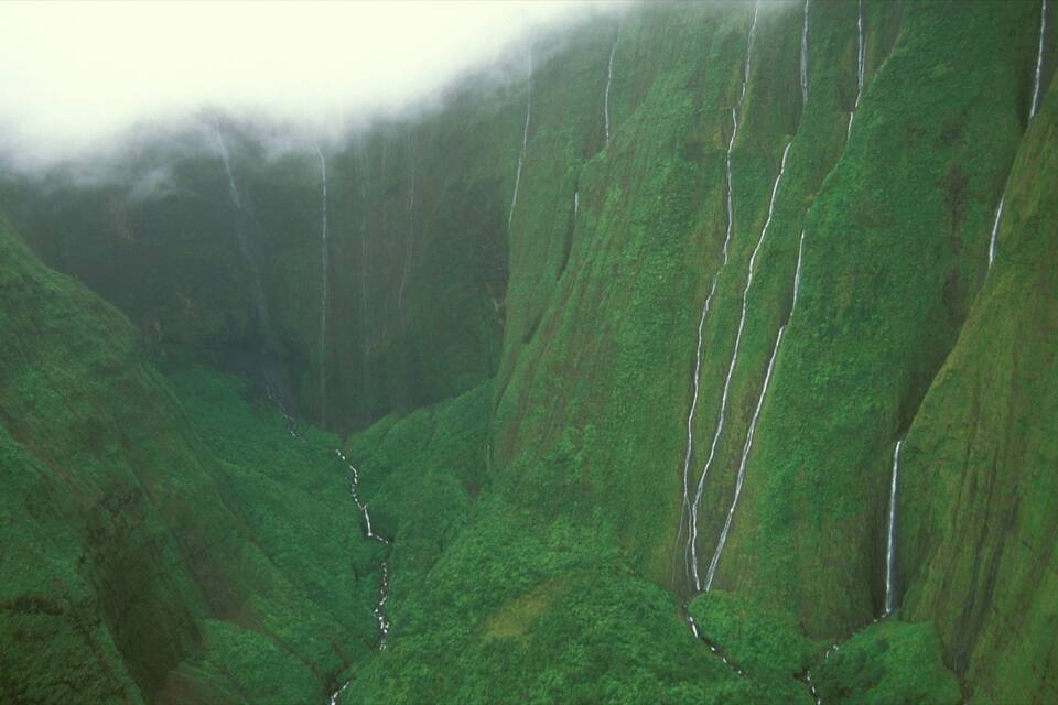 A lush green valley with steep cliffs and a river running through it.