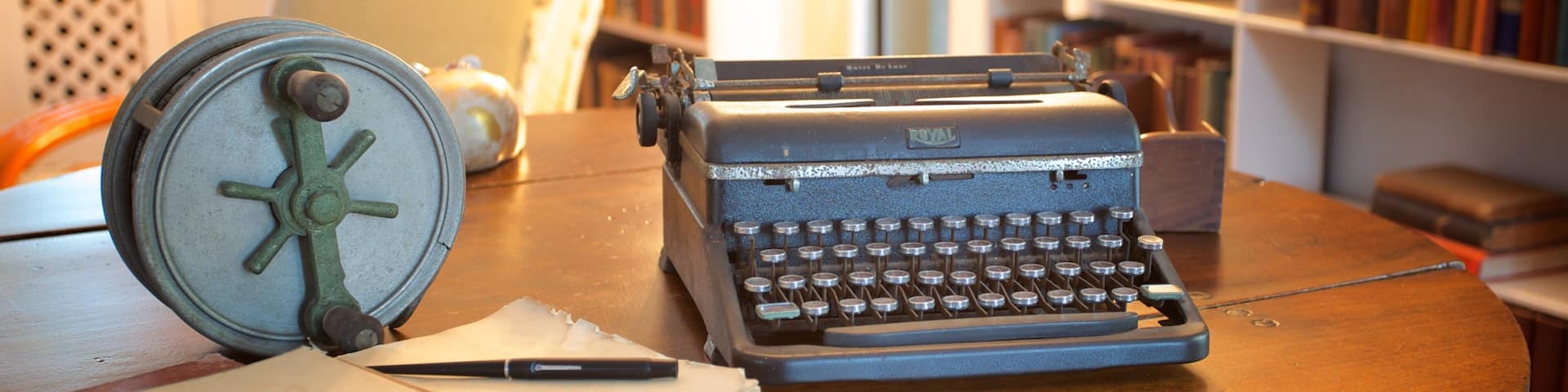 Una máquina de escribir antigua sobre una mesa de madera, junto a ella un cuaderno y un bolígrafo.