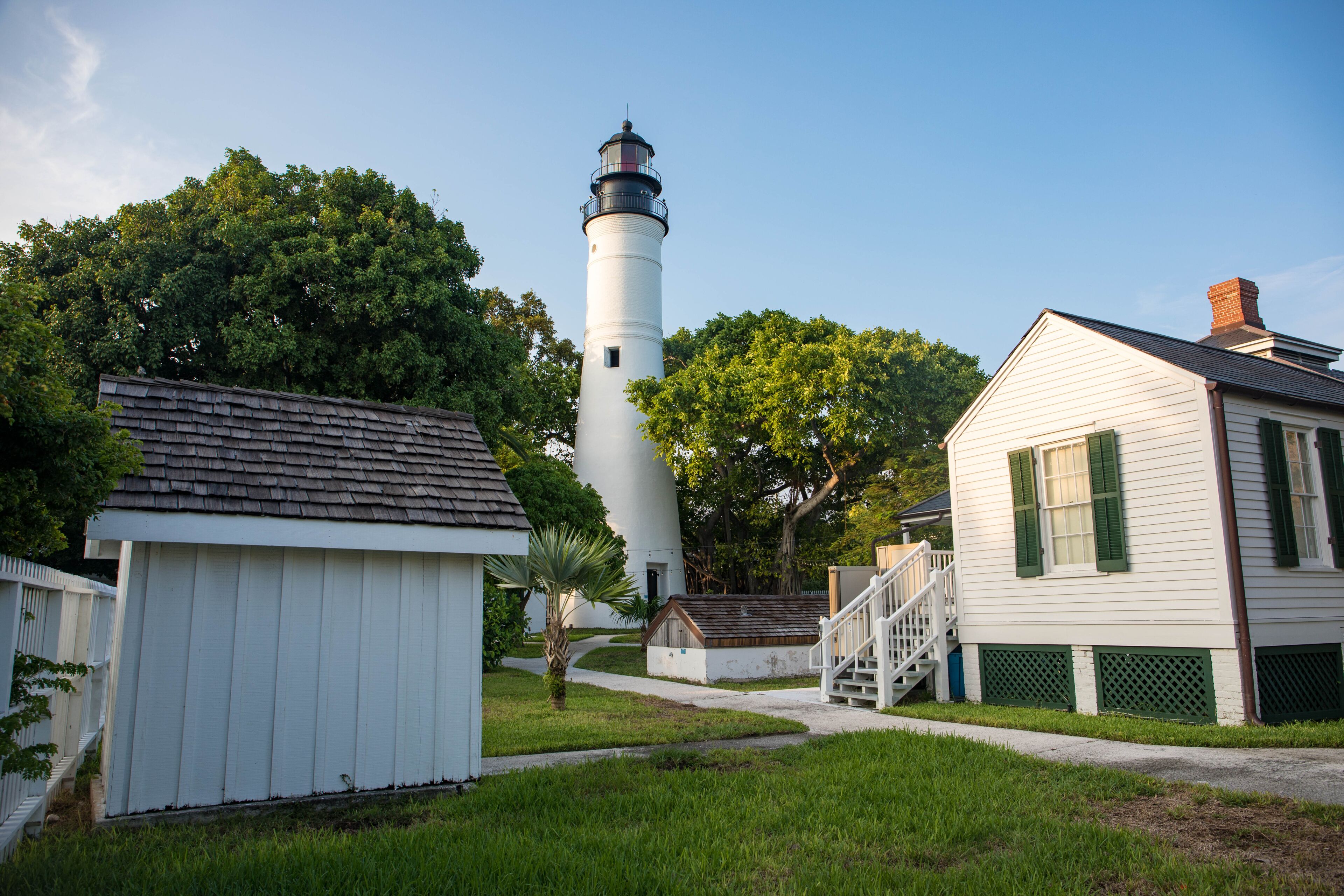 A lighthouse, a white building with green shutters, and a small white structure with a wooden roof.