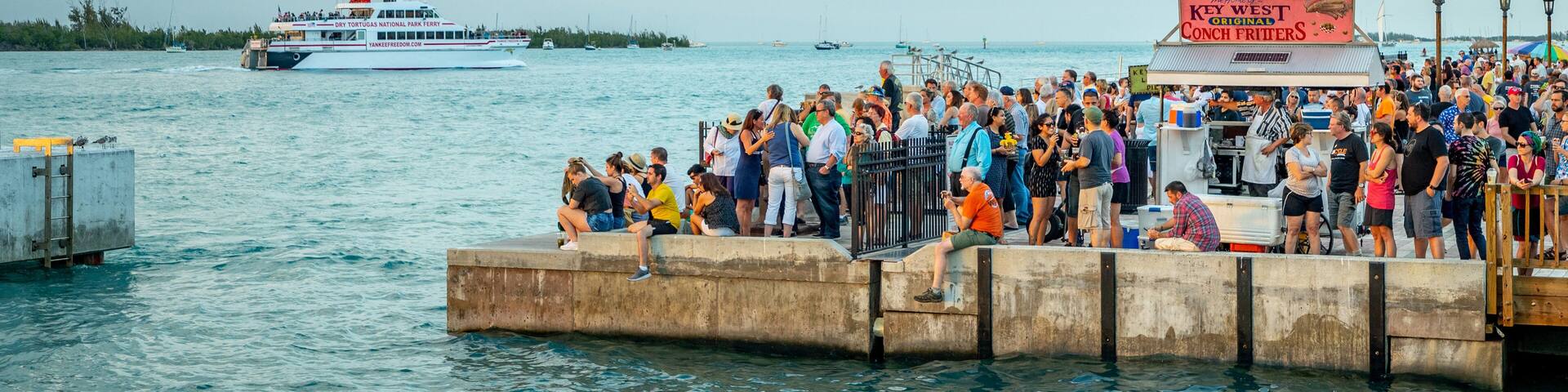 A crowded pier with a ferry and a restaurant named "The Original Conch Fritters."