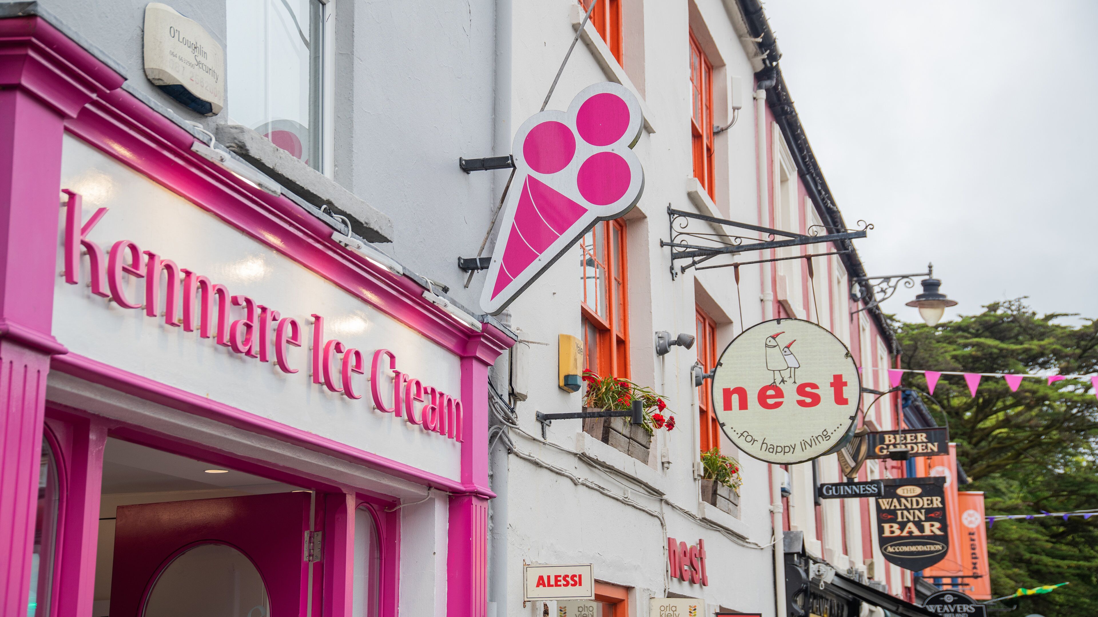 Fachada rosa com o nome Kenmare Ice Cream, um letreiro com a palavra 'nest' e uma ilustração de pássaro, e um letreiro de 'Beer Garden'.
