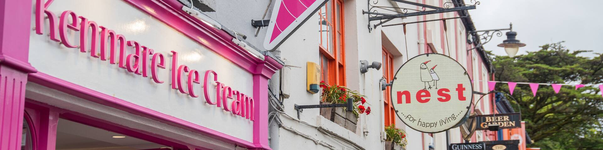 A pink storefront named Kenmare Ice Cream, a sign for 'nest' with a bird illustration, and a 'Beer Garden' sign.
