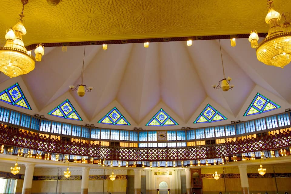 Un salón majestuoso con candelabros ornamentados, vidrieras de colores y celosías de madera intrincadas.