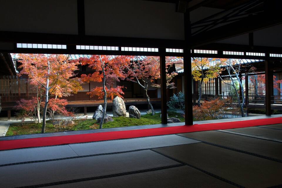Un jardí japonès tradicional amb vistes a la tardor, un fanal de pedra i un edifici de fusta.