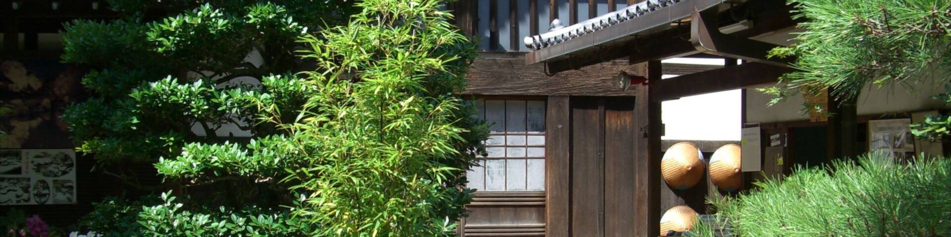 A traditional Japanese building with a wooden gate, surrounded by lush greenery and pine trees.