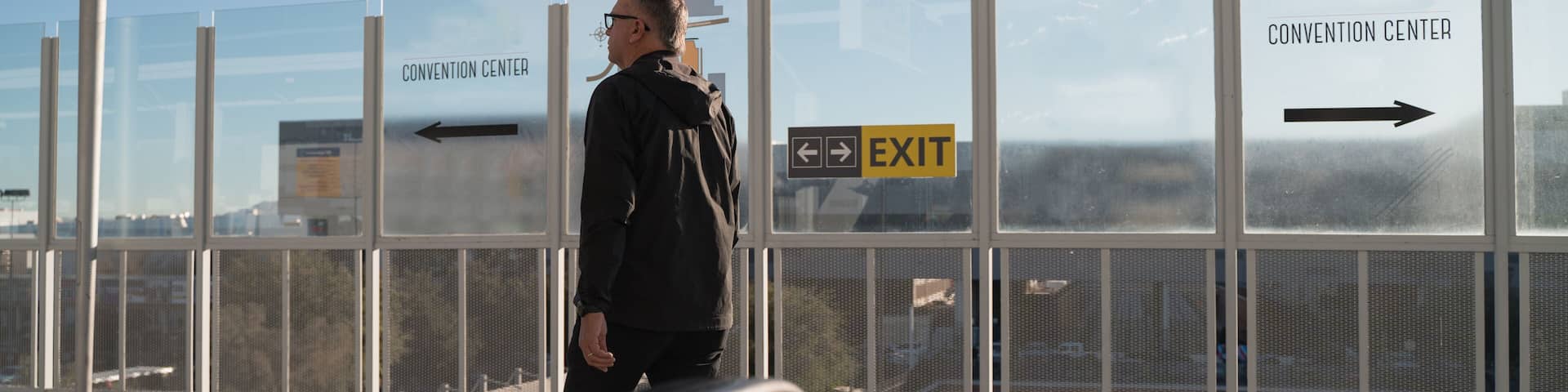 Una persona de pie cerca de una barrera de vidrio con señales direccionales que indican 'Convention Center' y 'Exit'.