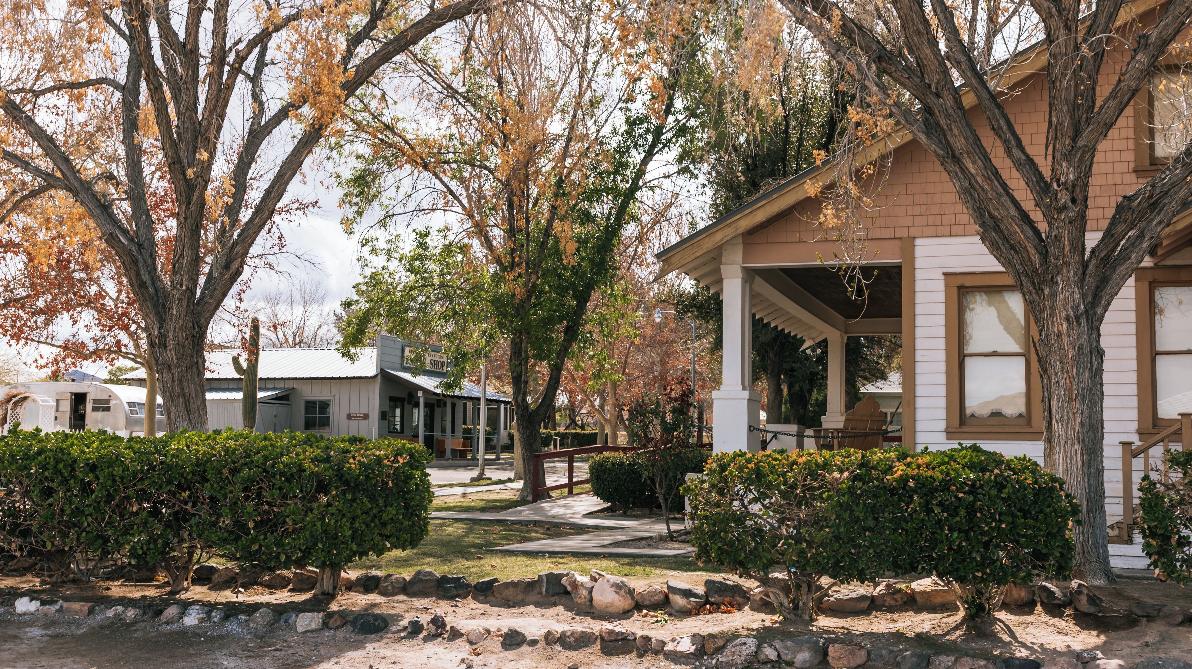 A residential area with a white house, a vintage trailer, and a covered porch.
