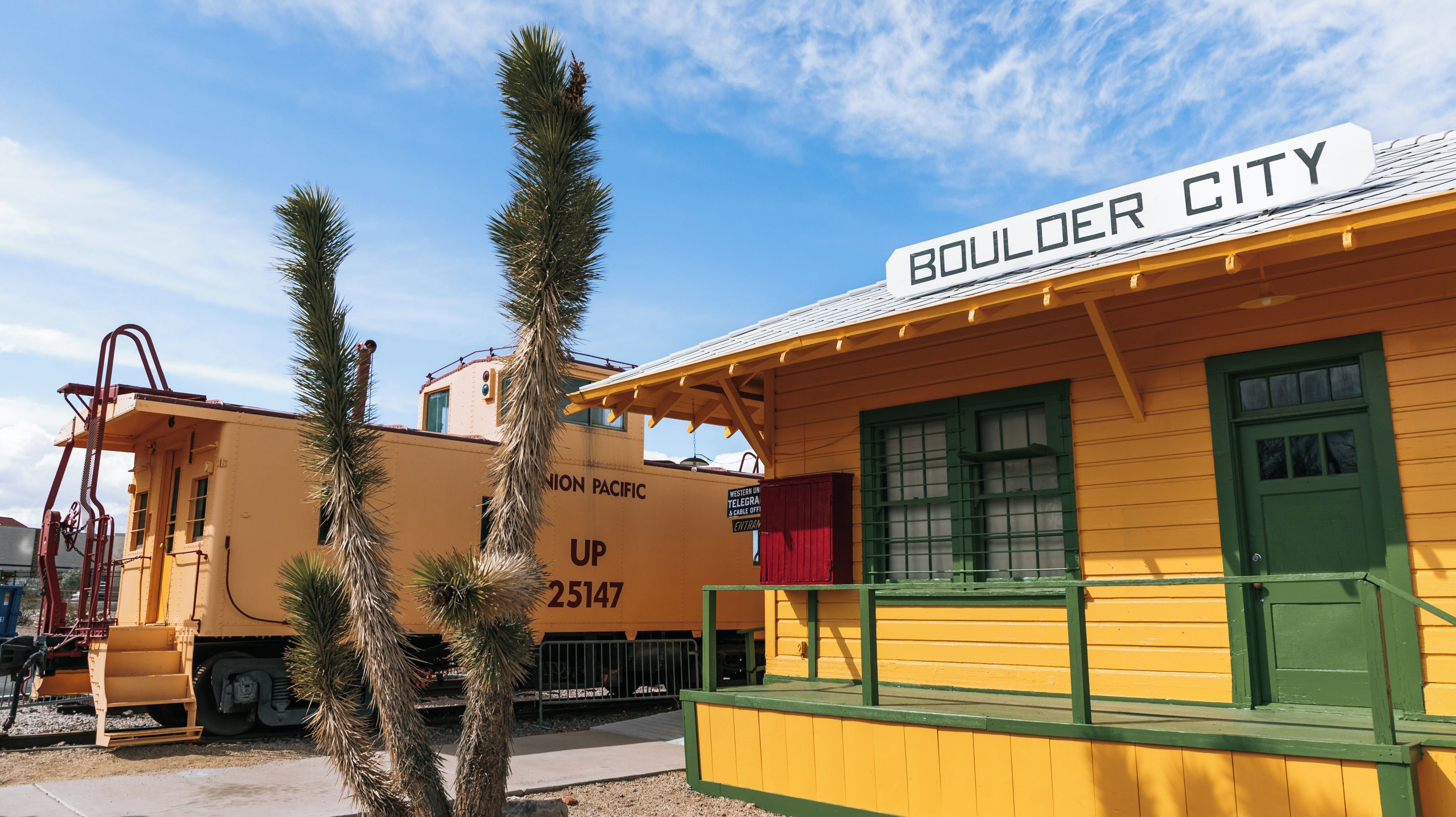 A yellow train car with 'Boulder City' and 'UP 25147' on it, a green door, and a sign for 'Western Union & Cable Office'.