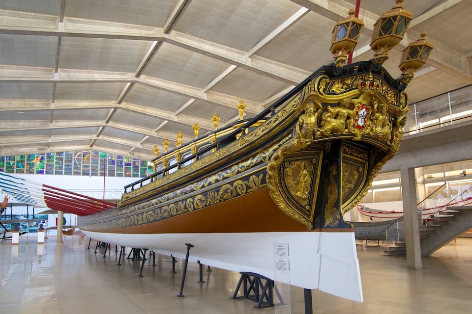 Un barco dorado expuesto en un museo con techo abovedado alto y ventanales de vidrio.