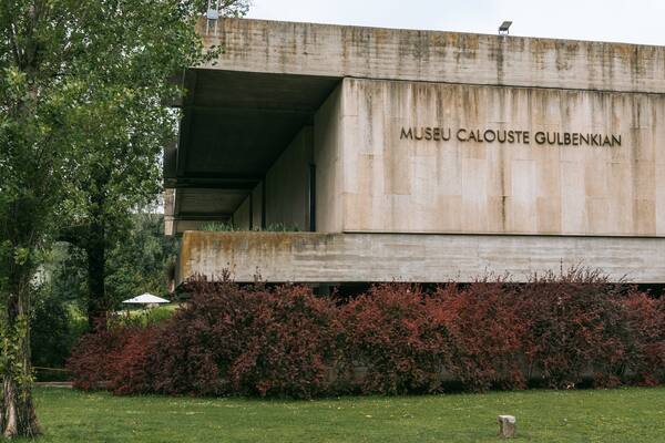Un bâtiment en béton sur lequel on peut lire l’inscription « MUSEU CALOUSTE GULBENKIAN » et un jardin environnant aux feuillages rouges.