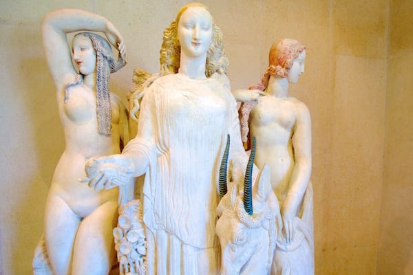 Uma escultura em mármore de uma mulher segurando uma criança, com outra figura ao fundo.