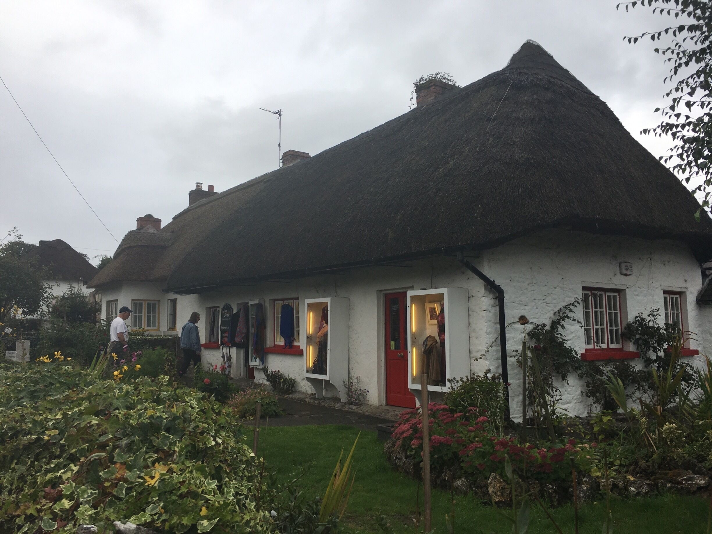 A white house with a thatched roof, a red door, and a garden with flowers and plants.