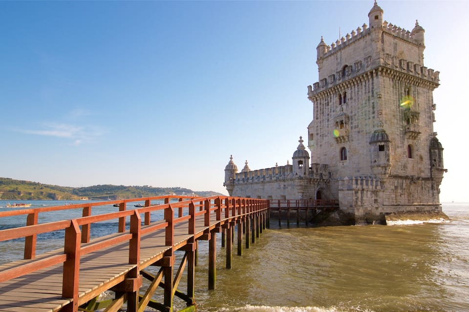 Un castillo de piedra histórico junto a un río, con un puente de madera que lo atraviesa.