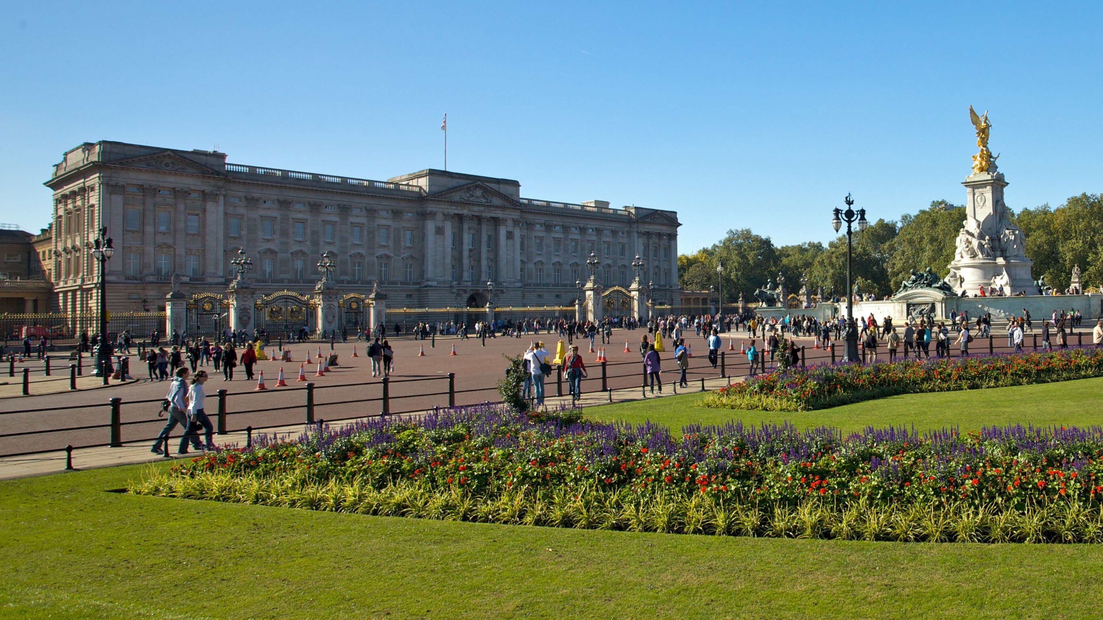 Buckingham Palace in London showcases its grandeur on a sunny day with crowds and vibrant gardens