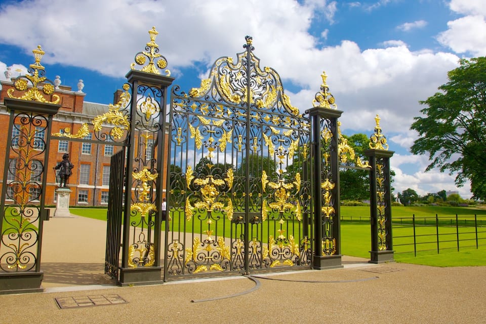 A wrought iron gate with gold accents, a statue, and a red brick building in the background.