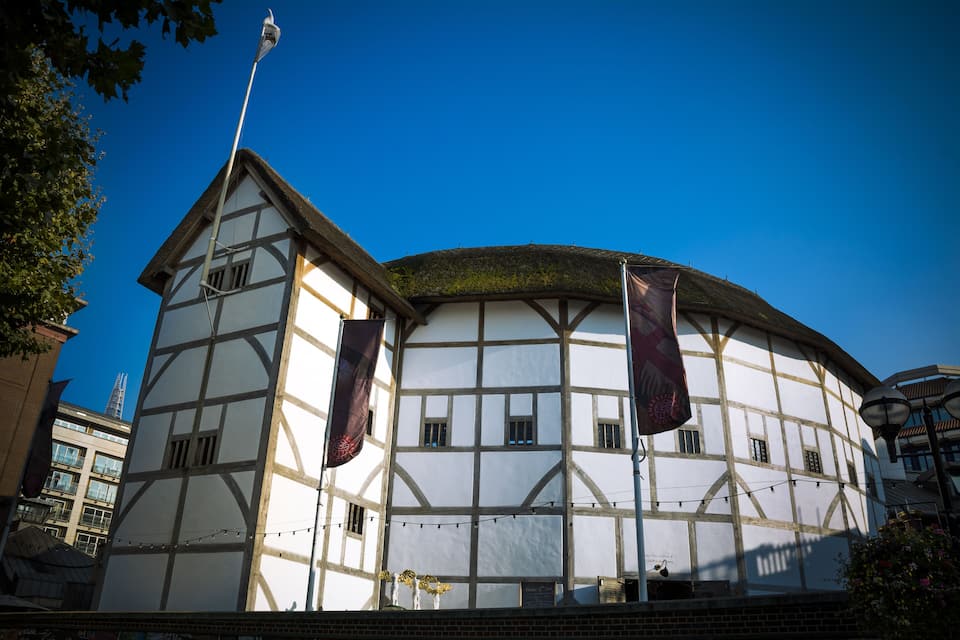 A historic building with a white facade and timber framing, featuring two flags and a thatched roof.