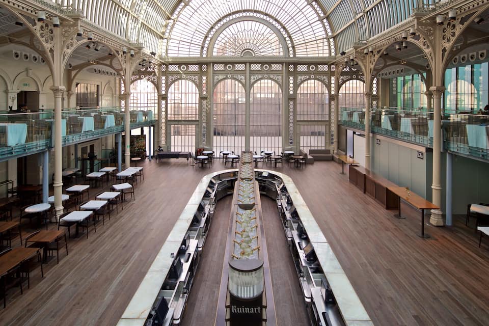 An ornate glass-domed interior with wooden tables and benches.