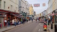 A busy street with shops, pedestrians, and a Union Jack flag.