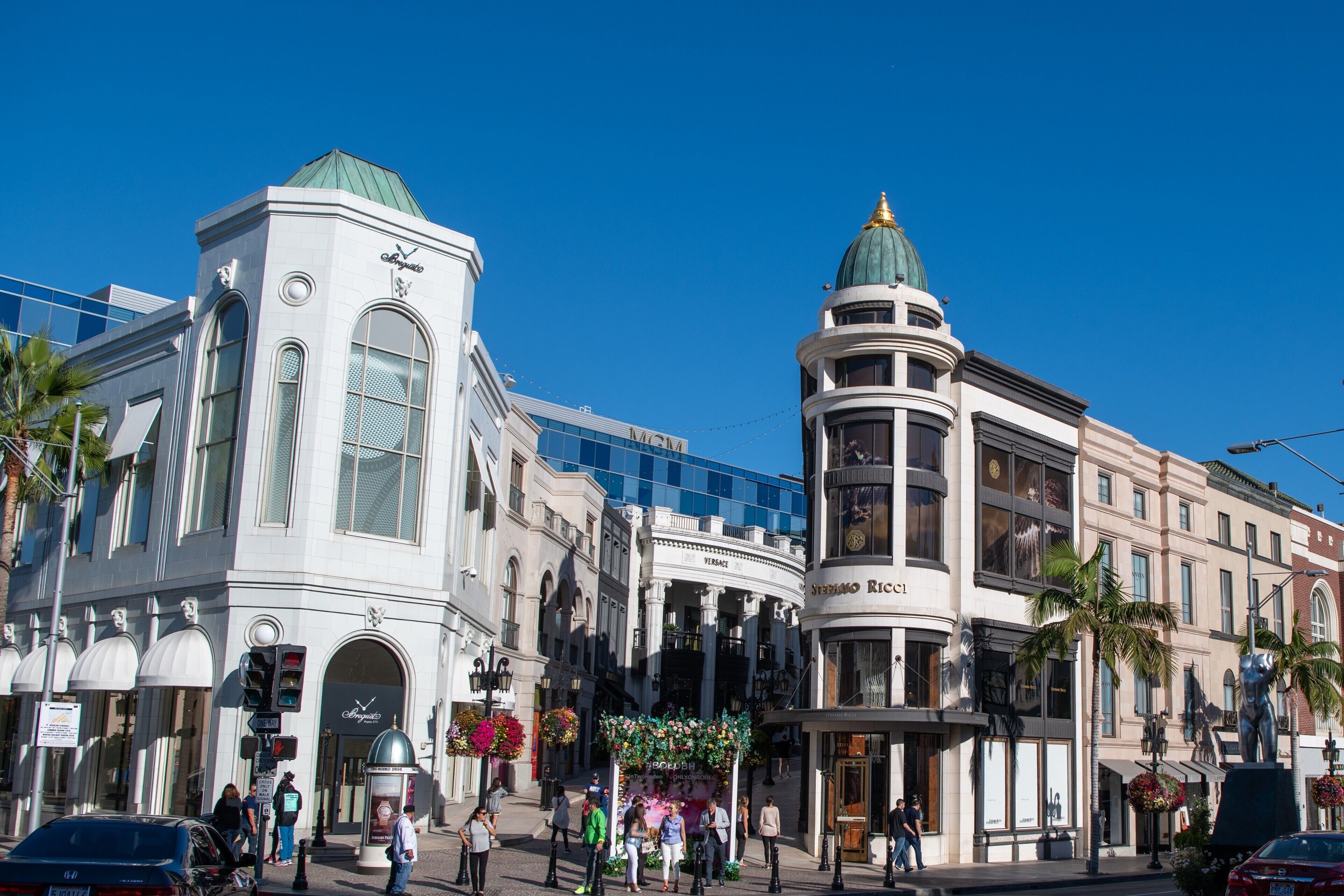 A busy urban street with historic buildings, including a prominent white building with a green dome and another with a curved facade.