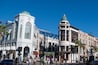 A busy urban street with historic buildings, including a prominent white building with a green dome and another with a curved facade.